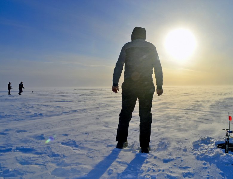 Un homme debout sur un étant de pêche gelé avec un levé du soleil